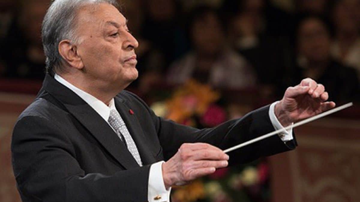 Elderly conductor leading orchestra with baton.